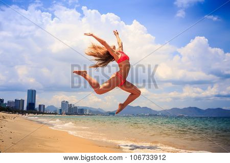 Blonde Slim Gymnast In Bikini In Jump Over Beach Against Sky