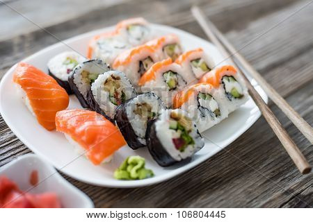 various Japanese sushi on white plate with chopsticks on wooden background