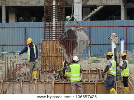 Construction workers pouring concrete slurry into ground beam formwork