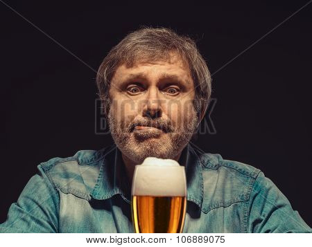 The spellbound man in denim shirt with glass of beer