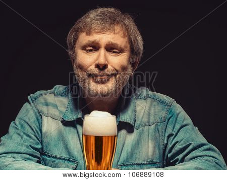 The spellbound man in denim shirt with glass of beer