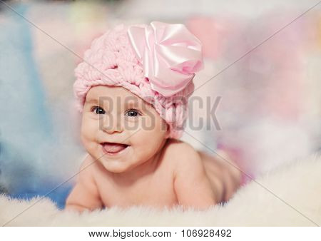 Smiling Baby Girl In A Pink Knited Hat Lying On The Blanket
