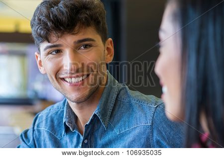 Portrait of happy young man looking his girlfriend and smiling. Couple loving eachother indoor. Shallow depth of field with focus on handsome young man smiling.
