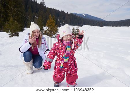 happy family on winter vacation, mom and cute little girl have fun and slide while snow falkes falling