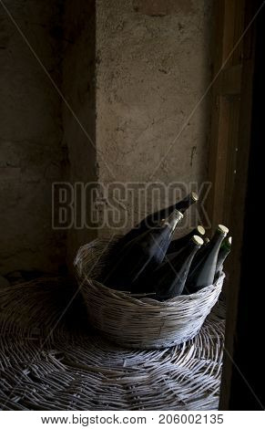 old and dusty botlles of aged red wine in a wicker basket illumined through a window