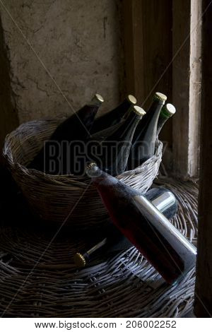 old and dusty botlles of aged red wine in a wicker basket illumined through a window