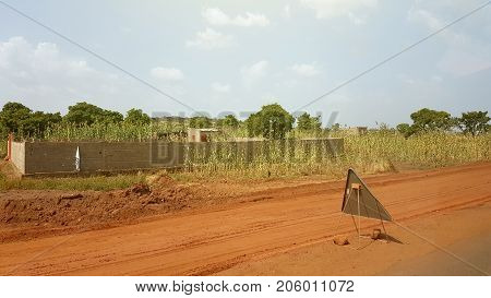 Generic poor house and street sign in Bamako Mali with small house near the red African soil highway