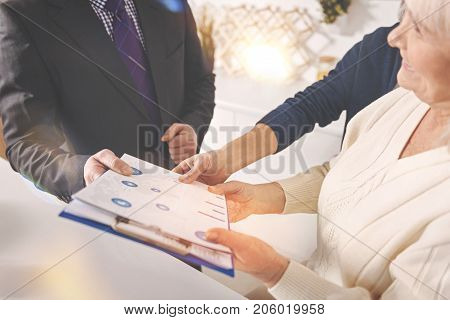 Some tips. Close up of folder in hands of a professional insurance agent while consulting positive retired couple at home