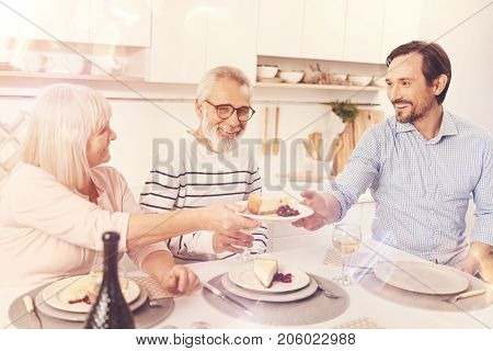 Home made. Positive aged parents and their son sitting at the table and enjoying dinner together at home