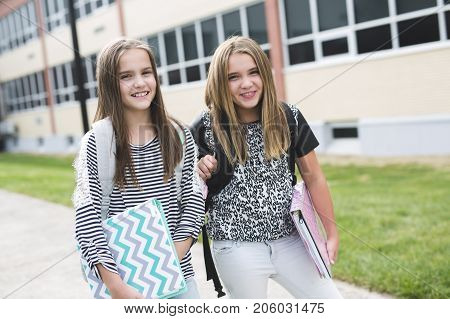 Portrait of two pre teenage girls studying outdoors in school yard