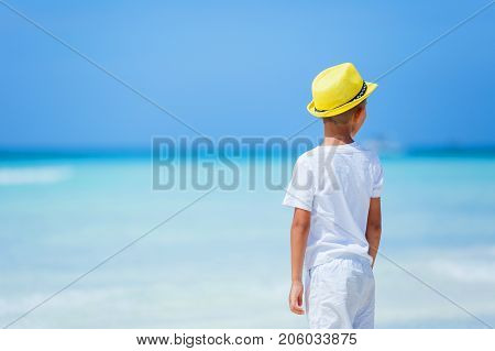 Back viewi lttle boy wearing white having fun on tropical ocean beach. Kid during family sea vacation. Summer water fun.