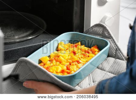 Woman taking out baking dish with dinner from microwave oven. Cooking for one concept