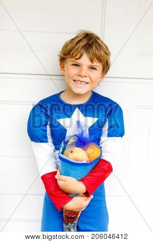 Happy little kid boy in superhero costume on his first day to school . Child outdoors on warm sunny day, Back to school concept. Kid as super hero with traditional schoolbag in German Schultuete