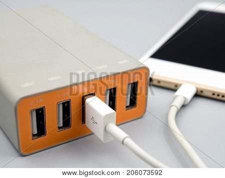 Close-up image of smart phone charging with multiport USB power adaptor on gray background Selective focus