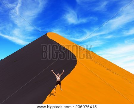 The man enthusiastically jumps on the crest of the dune. Purple and yellow dune of the Namib desert. Sunset. The concept of extreme and exotic tourism