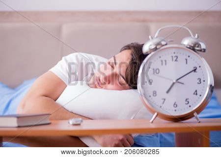 Man in bed frustrated suffering from insomnia with an alarm cloc