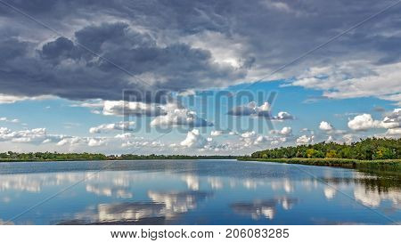 Colorful forest with green yellow trees and raining sky reflected in water surface lake river . Sunny sky with grey clouds. autumn sky after rain.