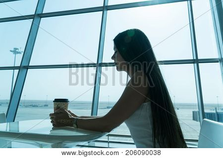 Girl Is Holding A Glass Of Coffee In Airport's Business Lounge With Aircraft