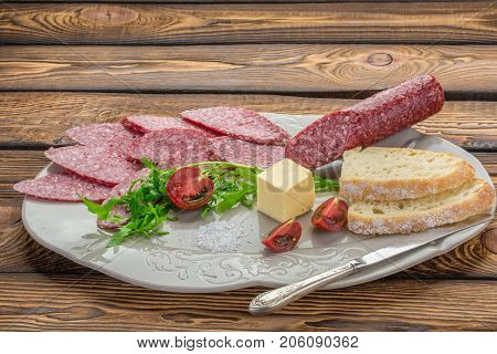 raw smoked sausage salami on white plate knife. Ingredients for sandwiches with sausage thyme herbs tomatoes white bread butter over wooden background