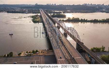 Aerial top view of automobile and railroad Darnitsky bridge across Dnieper river from above, Kiev (Kyiv) city sunset skyline, Ukraine