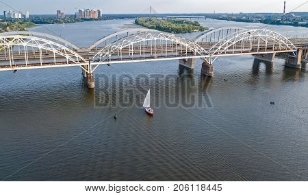 Aerial top view of Darnitsky bridge, yachts and boats sailing in Dnieper river from above, Kiev (Kyiv) city skyline, Ukraine