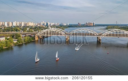 Aerial top view of Darnitsky bridge, yachts and boats sailing in Dnieper river from above, Kiev (Kyiv) city skyline, Ukraine