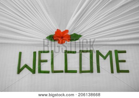 Floral decor and word WELCOME on bed in hotel room, closeup