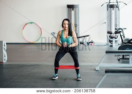 cute fit girl performs modern leg exercises with elastic rubber