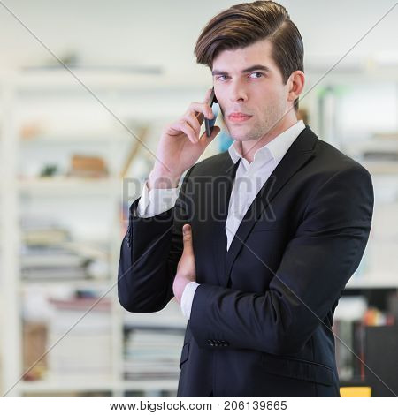 Portrait of hansome business man in office talking on mobile phone and looking at camera