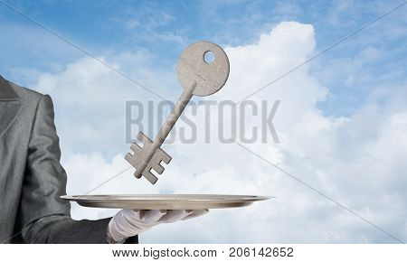 Closeup of waiter's hand in white glove presenting stone key symbol on metal tray with blue cloudy skyscape on background. 3D rendering.