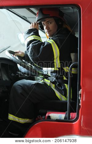 Portrait of fireman wearing fire fighter turnouts, sits behind wheel of fire engine