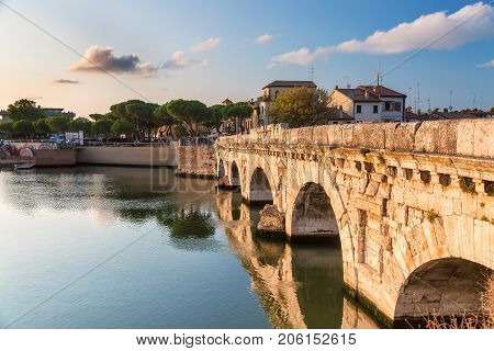 Historical roman Tiberius bridge over Marecchia river during sunset in Rimini Italy