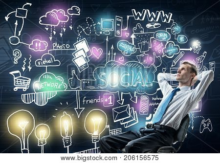 Young businessman sitting on chair with hands on head and socia communication concept on wall