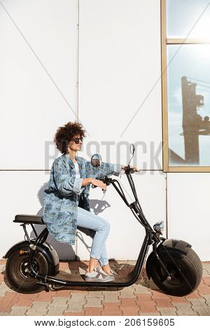 Stylish young woman sitting on a modern motorbike outdoors