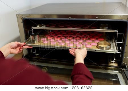 cooking, baking and people concept - chef with macarons on oven tray at bakery or confectionery