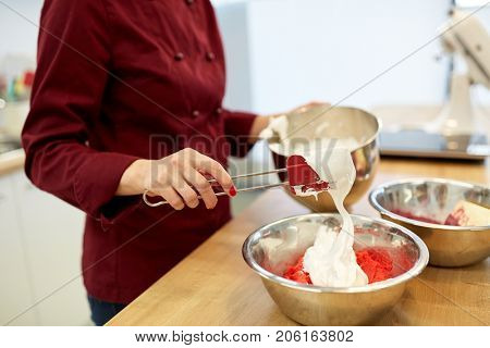cooking, food and people concept - chef adding whipped egg whites to macaron batter in bowl at pastry shop kitchen