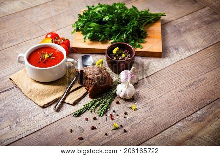 Red ukrainian borsch with sour, garlic, parsley, spices and a lot of dill and parsley on a wooden background. Copy space. Close-up of appetitzing dish. Food concept.
