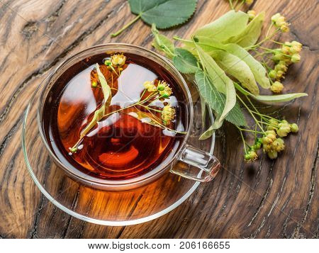 Cup of linden tea and lime flowers on the wooden table.