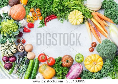 Colorful vegetables arranged in frame on light grey stone background, copy space for text in the middle, selective focus
