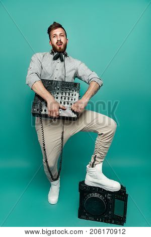 Young trendy male posing with portable mixing console and looking at camera on green isolated studio background.
