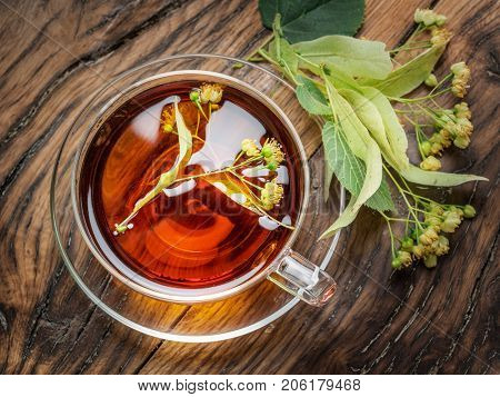 Cup of linden tea and lime flowers on the wooden table.