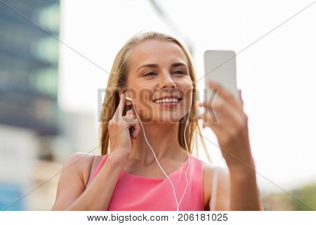 technology, lifestyle and people concept - smiling young woman with smartphone and earphones listening to music and taking selfie in city