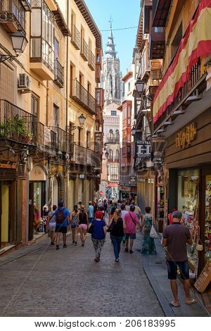 TOLEDO,SPAIN - AUGUST 8,2017 : Tourists on a narrow street on the medieval city of Toledo in Spain with the Cathedral belfry on the background