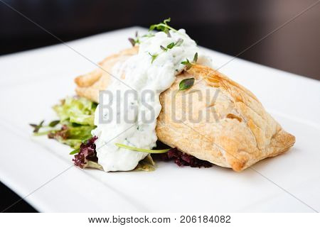 Traditional russian pie - coulibiac. Baked puff pastry filled with smoked salmon, served with sour cream sauce