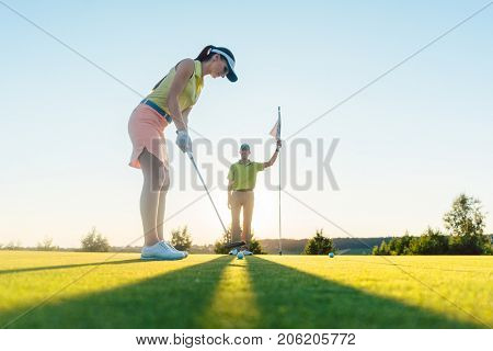 Low-angle side view of an attractive fit woman exercising hitting technique during golf class with an experienced professional player in summer