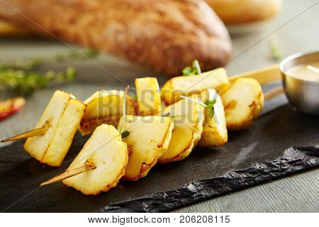 Hot appetizer - fried cheese halumi on wooden stick on black stone against of blurry bread. Gastronomic restaurant menu