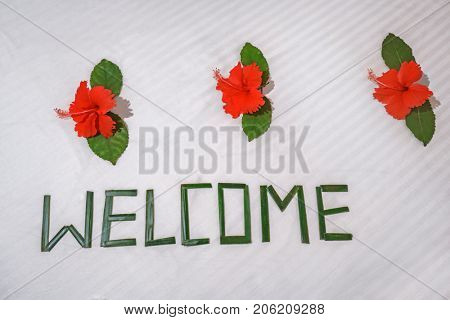 Word WELCOME and beautiful flowers on bed in hotel room