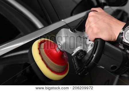 Man polishing car with power buffer machine in repair shop