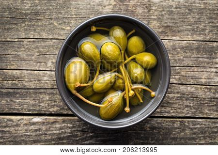 Pickled caper berries in bowl on old wooden table.