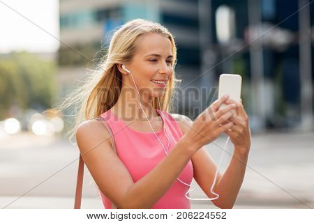 technology, lifestyle and people concept - smiling young woman with smartphone and earphones listening to music and taking selfie in city
